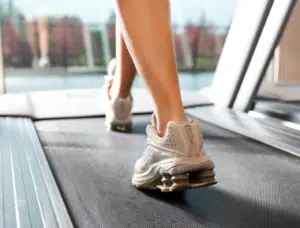 Close-up of legs in white sneakers walking on a treadmill, promoting the BetterTogether weight loss challenge with friends.