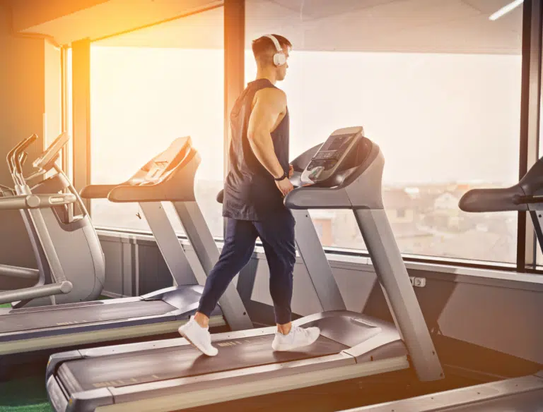 Person in athletic gear walking on treadmill with headphones, promoting BetterTogether weight loss challenge with friends.