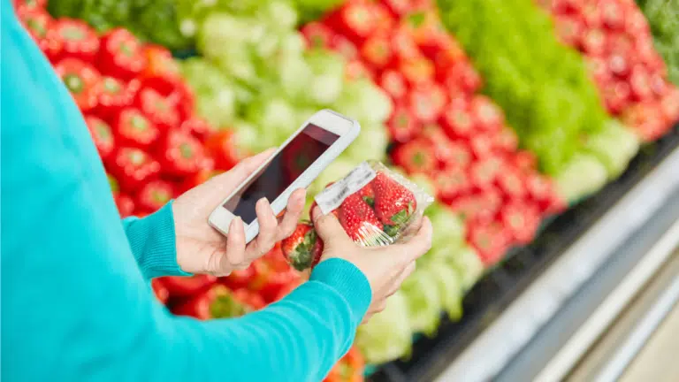 Join BetterTogether Weight Loss Challenge: Friend holding strawberries & phone in grocery store, promoting healthy choices.